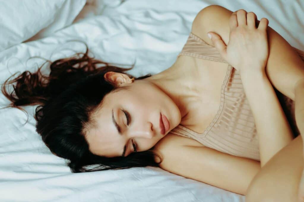 Woman laying down and holding her shoulder in bed