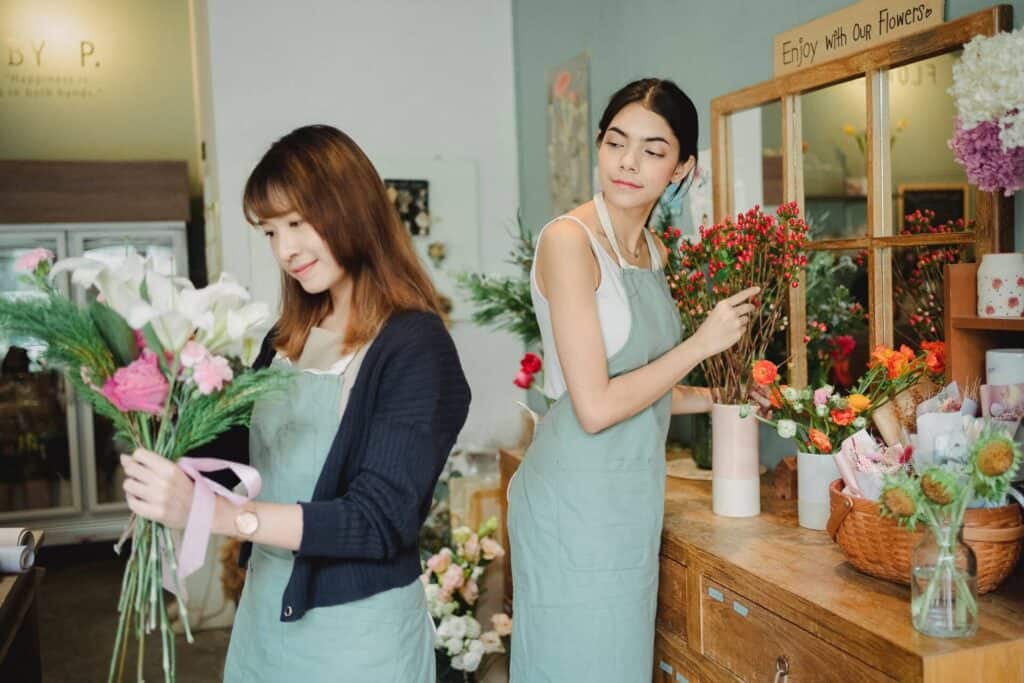Two women working at a flower shop and one is looking over the other's shoulder