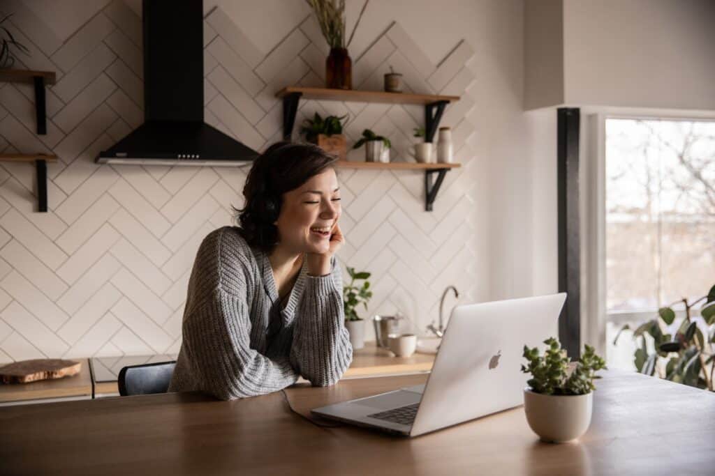 Woman laughing at laptop in kitchen