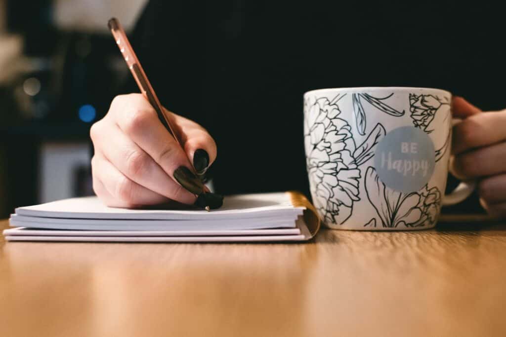 Woman writing in book with coffee mug beside it